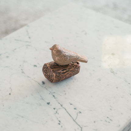 De urn is gemaakt van keramiek en heeft de kleur brons. De urn is een vogeltje die staat op een kleine boomstronk. De urn staat gestationeerd op een wit marmeren blad.