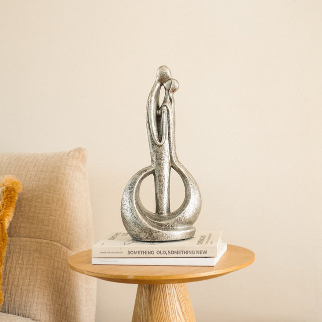De urn is gemaakt van keramiek en heeft de kleur silver. De urn is een kussend koppel. De urn staat gestationeerd op een klein rond tafeltje naast de bank. 