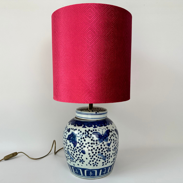 Urn beschildert in delfts blauwe stijl met vlinders. Boven op de urn is een lamp met een roze kap.